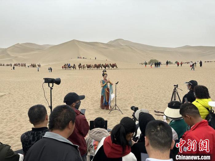 圖為2023年4月底，敦煌大漠“逐舞者”奧楠在鳴沙山月牙泉景區(qū)視頻直播，吸引游人圍觀?！●T志軍 攝